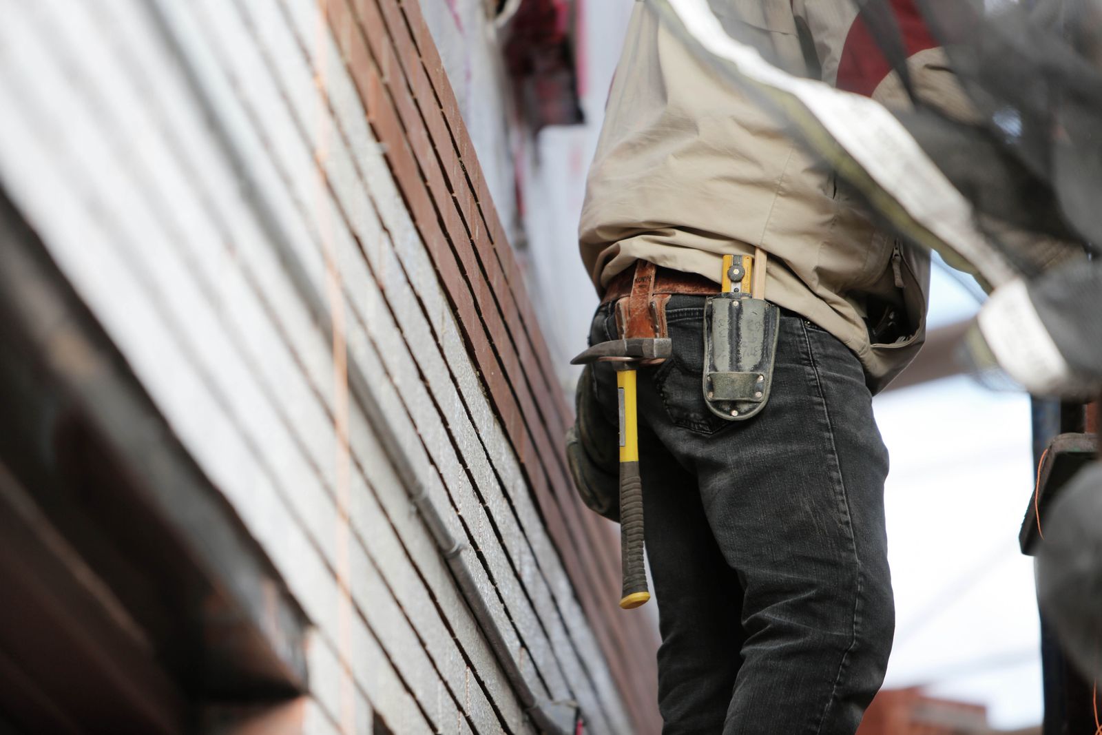 A handyman in a tool belt with a hammer working on the exterior of a St. George home